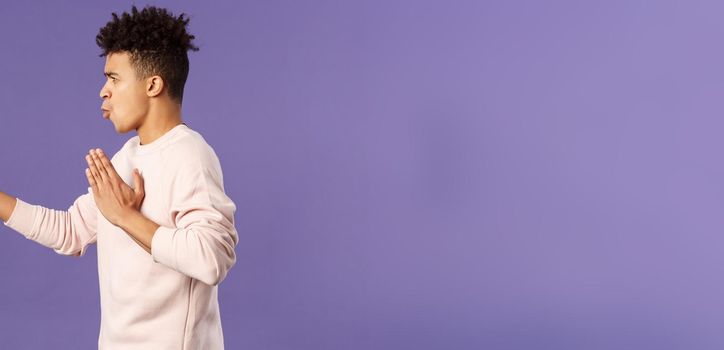 Profile portrait of young hispanic guy with dreads acting like he is ninja or martial arts fighter, practice his kung-fu or taekwondo skills, standing purple background. Copy space