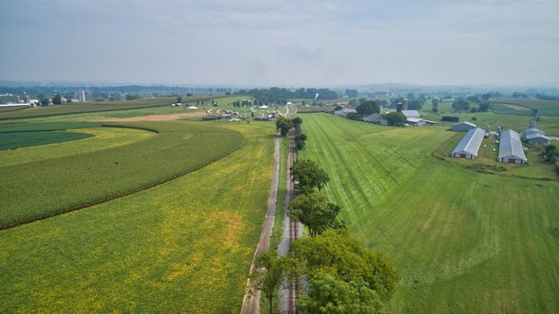 Drone View of Amish Countryside With Barns and Silos and a Single Railroad Track Traveling Through It, on Sunny Day.