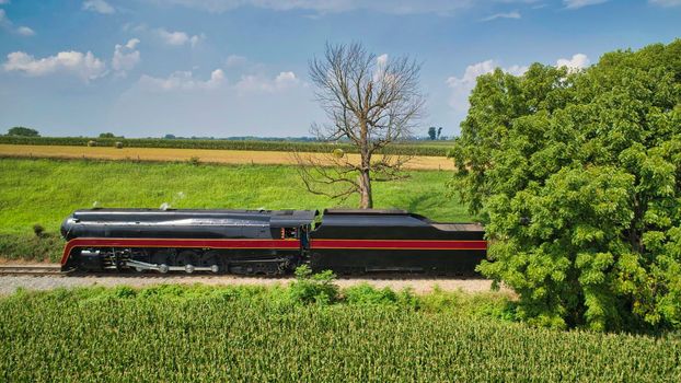 Drone Side View of an Antique Steam Engine, Approaching, Blowing Steam and Traveling Along the Countryside on a Sunny Day