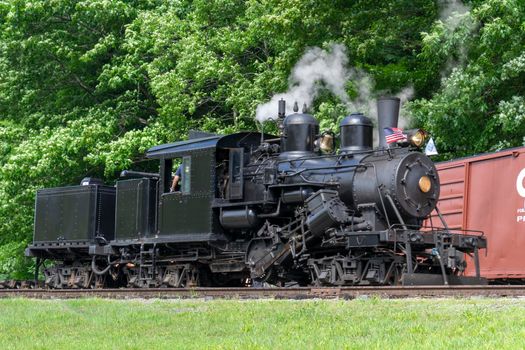 A View of a Antique Shay Steam Engine Moving Slowly Blowing Smoke and Steam on a Sunny Day