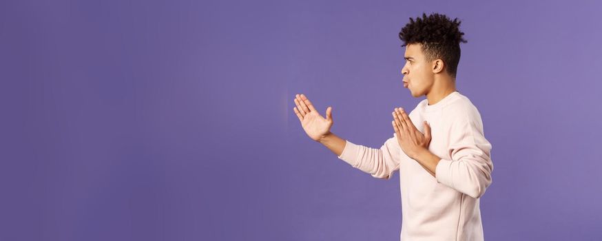 Profile portrait of young hispanic guy with dreads acting like he is ninja or martial arts fighter, practice his kung-fu or taekwondo skills, standing purple background. Copy space