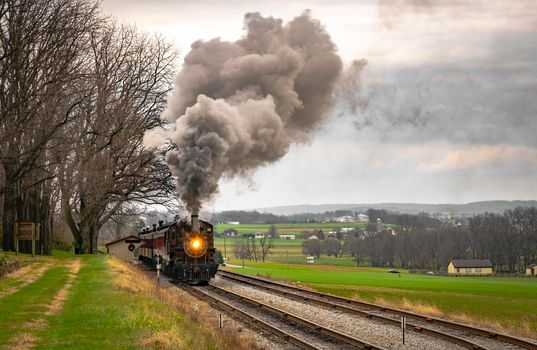 Ronks, Pennsylvania, December 2020 - An Antique Steam Passenger Train Traveling Thru Farmlands Puffing Lots of Smoke on a Cloudy Winter Day