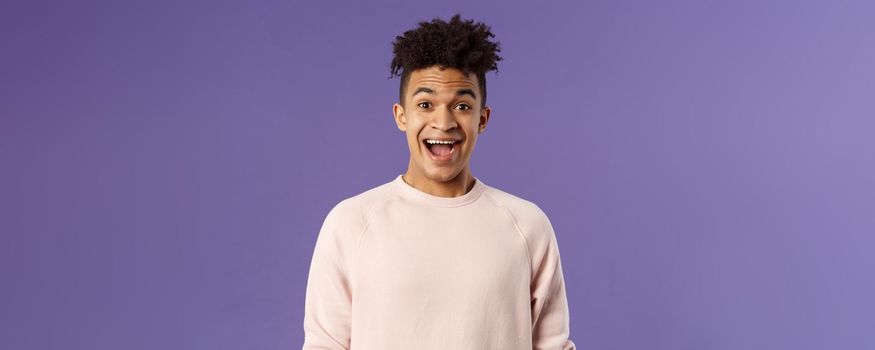 Close-up portrait of enthusiastic, excited and surprised hispanic guy hear amazing news, open mouth beaming smile from amazement and joy, rejoicing glad for friend achievement, purple background.