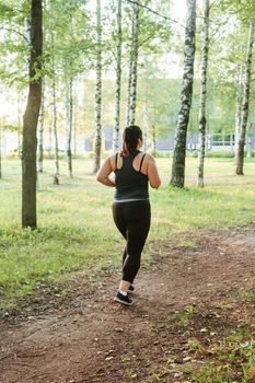 A charming brunette woman plus-size body positive practices sports in nature.