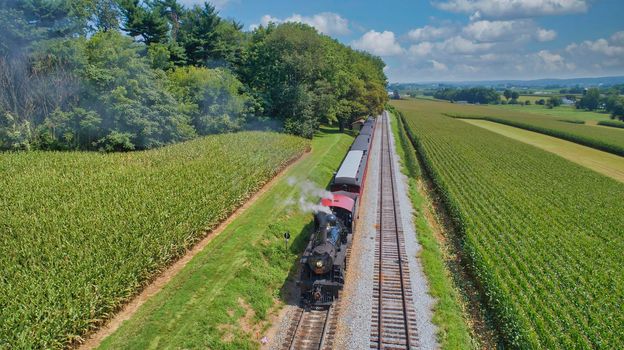 Drone View of an Antique Steam Engine, Approaching, Blowing Steam and Traveling Along the Countryside on a Sunny Day