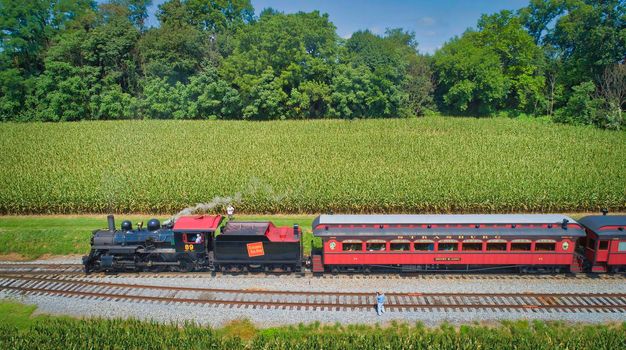 Ronks, Pennsylvania, August 29, 2021 - Drone View of an Antique Steam Engine, Approaching, Blowing Steam and With on Lookers Taking Photos on a Sunny Day