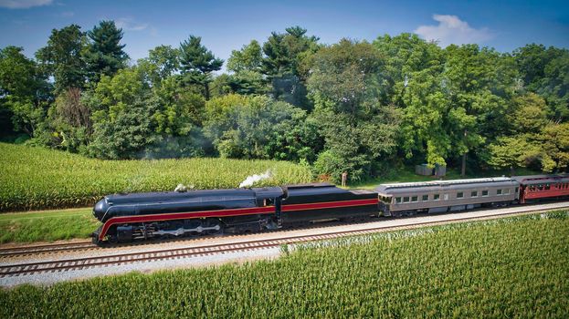 Drone View of an Antique Steam Engine, Approaching, Blowing Steam and Traveling Along the Countryside on a Sunny Day