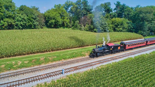 Ronks, Pennsylvania, August 28, 2021 - Drone View of an Antique Steam Engine, Approaching, Blowing Steam and With on Lookers Taking Photos on a Sunny Day