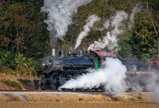 Ronks, Pennsylvania, November 8, 2021 - A View of a Restored Steam Freight Train Blowing Smoke and Steam Traveling Along a Rural Countryside on a Sunny Day