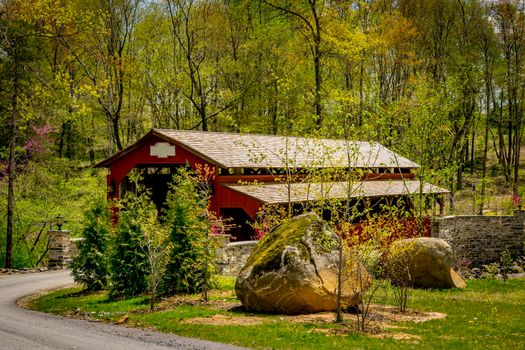 View of a Country Road Approaching to a Restored Covered Bridge on a Sunny Spring Day