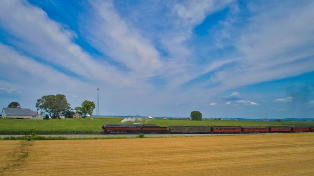 Aerial View of a Steam Passenger Train Approaching, Traveling Through Farmlands, With Corn and Wheat Fields, on a Beautiful Sunny Day.