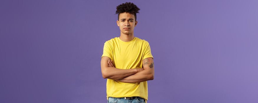 Close-up portrait of skeptical, unimpressed young man with dreads, look judgemental and uninterested, cross arms chest, go on impress me, smirk disappointed, purple background.