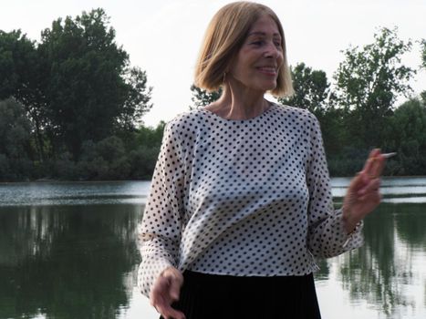 female pensioner having fun and smoking a cigarette in a park - aging free and wellness concept