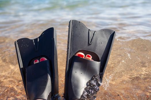 A woman in black flippers splashes near the shore. Fins stick out of the water. Swimming equipment. Summer holidays, fun, exploring the sea world concept. Space for copy.