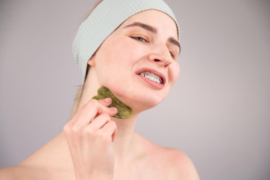 Portrait of a young woman massages her face with a gouache scraper on a white background