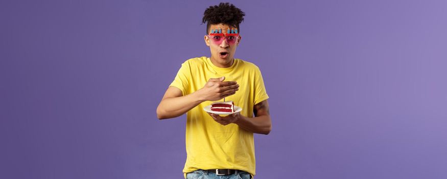 Celebration, party and holidays concept. Portrait of happy funny, enthusiastic young man celebrating birthday, protect lit candle on b-day cake from wind, making wish, smiling cheerful.