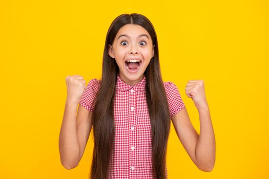 Amazed teen girl. Excited expression, cheerful and glad. Teenager child doing winner gesture celebrate clenching, say yes isolated on yellow background, studio portrait