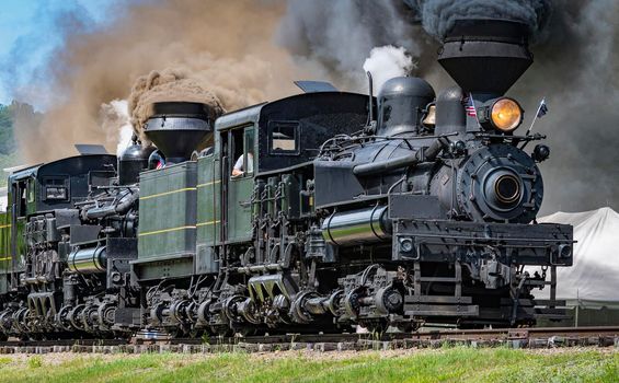 View of Two Shay Steam Engines, Heading Out for a Parade of Steam With the Two Engines Connected Together Blowing Black Smoke and White Steam on a Sunny Summer Day