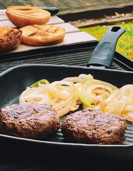 Cooking minced beef burger on cast iron grill skillet outdoors, red meat on frying pan, grilling food in the garden, English countryside living concept