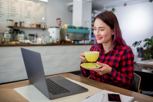 Young woman with pink hair with laptop computer sitting in cafe, intelligent female student working on net-book after her lectures in University