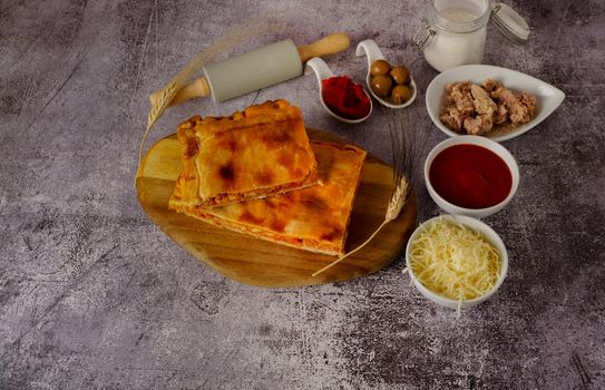 tuna empanada with all the ingredients separated in ceramic containers in the bottom of a red brick wall