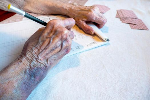 A bruise after an unsuccessful fall on the hands of an elderly man. Old age. wrinkled skin. an elderly woman with bruises on her hands is playing cards, keeping score. write the score in a card game