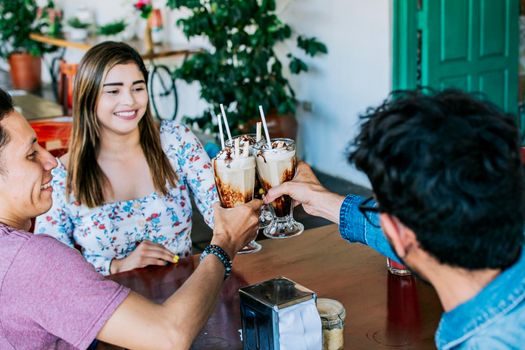 Three smiling best friends meeting and toasting in a coffee shop, Happy young friends toasting in a coffee shop. Happy friends enjoying a milkshake in a coffee shop