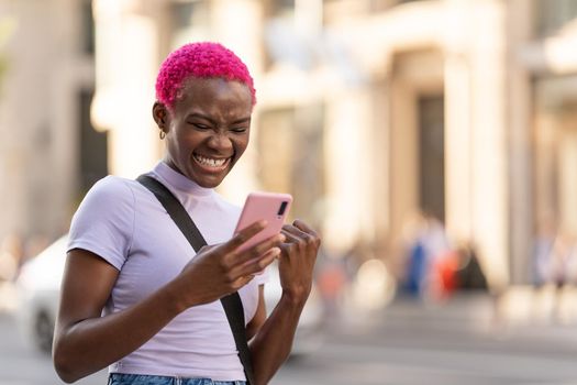 African young woman gesture victory with hand while using the mobile and laugh outdoors