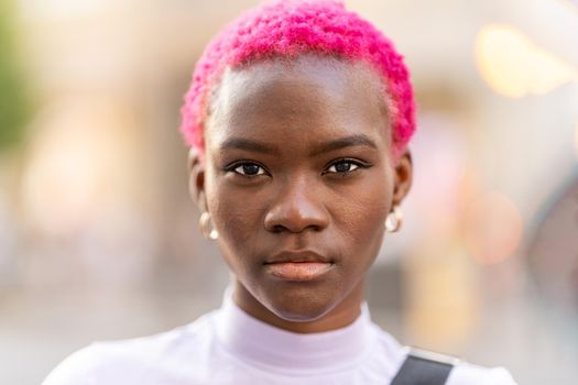 Portrait of a young stylish afro woman with short pink hair in a city