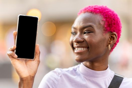 Smiling woman with short pink hair showing the screen of a mobile outdoors. Mockup concept