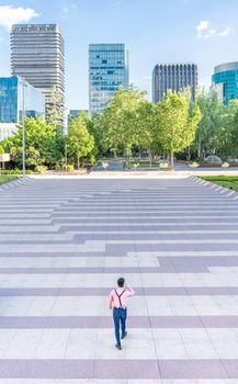 Vertical photo with top view of a man walking through an urban square surrounded by skyscrapers