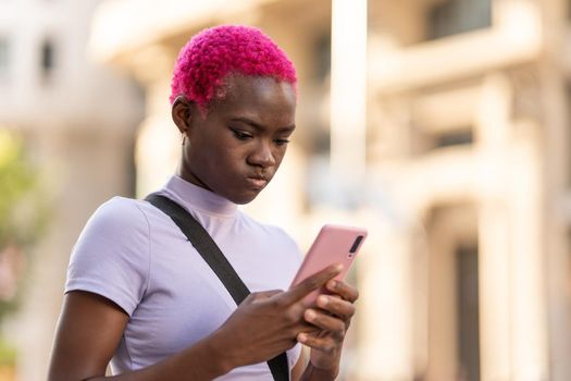 Portrait of an african young woman with serious expression using the mobile in the street