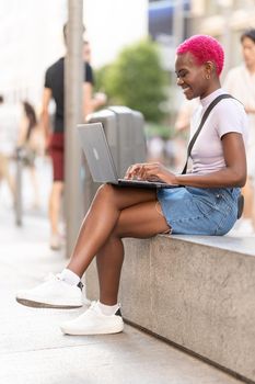 Vertical portrait of a stylish young african woman sitting on the street working with a laptop