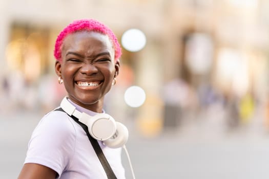 Afro young woman with pink short hair smiling to the camera in the street