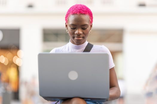 Portrait of a young african woman with pink short hair working with the laptop in the street