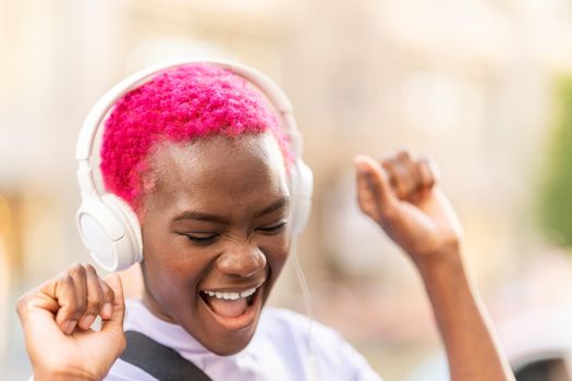 Close up portrait of an afro woman dancing while listening to music with headphones in the street