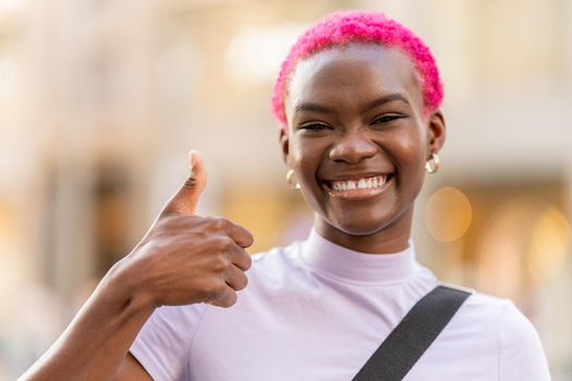 Smiling young african woman with pink short hair gesturing to be okay in the street