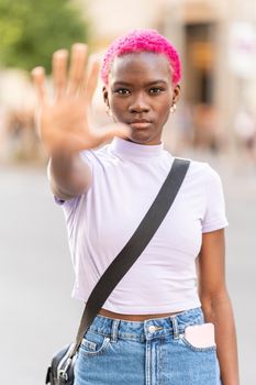 Vertical photo of a stylish african woman raising the hand to represent stop in the street