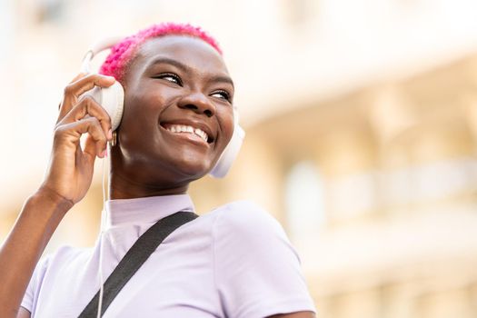 Stylish young afro woman smiling while using headphones on the street