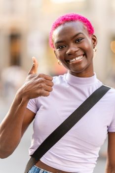 Young afro woman with short pink hair gesturing to be fine with the thumb raised outdoors