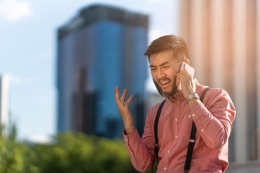 Asian businessman in shirt and braces talking on his mobile phone angrily while gesturing outdoors