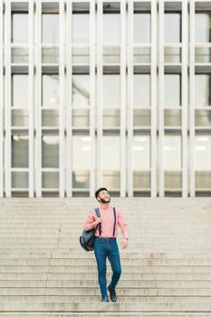 Asian man in casual clothes walking down a stairs with a business building in the background