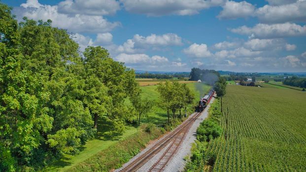 Drone View of an Antique Steam Engine, Approaching, Blowing Steam and Traveling Along the Countryside on a Sunny Day