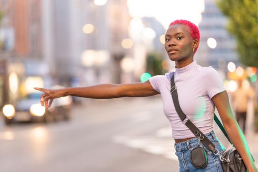 Stylish young african woman with short pink hair hairstyle hailing a taxi in the city