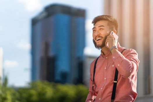 Photo with copy space of a stylish asian man talking to the phone with skyscrapers in the background