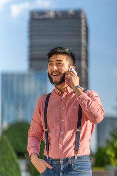 Vertical photo of a stylish asian man talking to the mobile with skyscrapers in the background