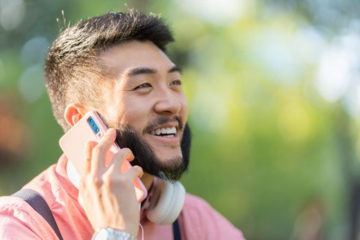 Portrait with focus on a happy asian man with casual clothes talking to the mobile in a park