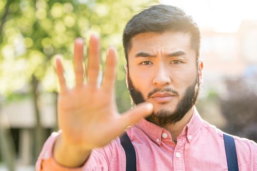 Sun illuminating an asian man in casual clothes gesturing stop with outstretched hand in a park