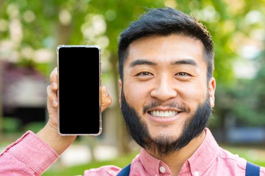 Portrait fo a happy chinese man showing the screen of a mobile phone while smiling