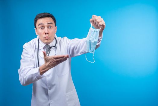 Male physician in white coat with stethoscope asking to put on medical mask while looking at camera against blue background